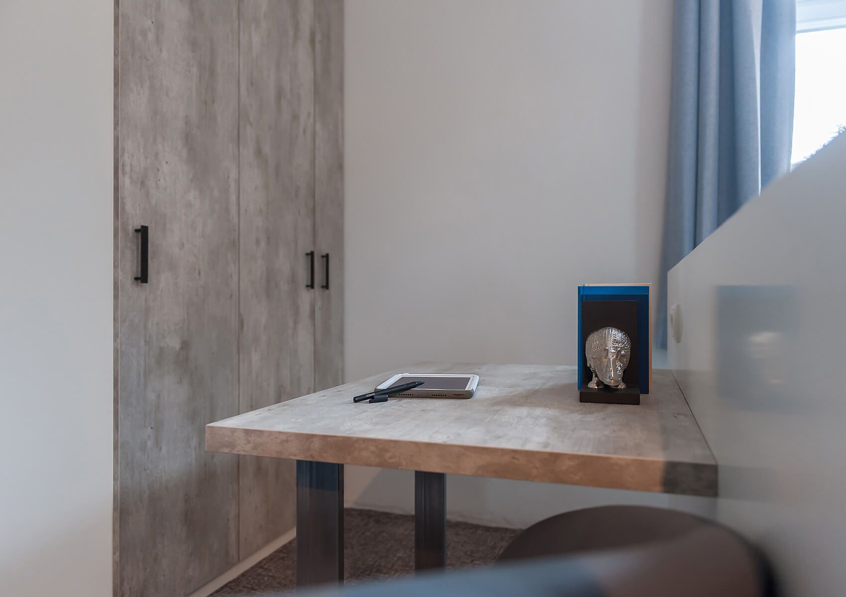 Una habitación pequeña con un armario de madera, una mesa con una computadora portátil y un bolígrafo, y un objeto decorativo sobre la mesa.