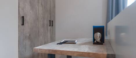 Una habitación pequeña con un armario de madera, una mesa con una computadora portátil y un bolígrafo, y un objeto decorativo sobre la mesa.