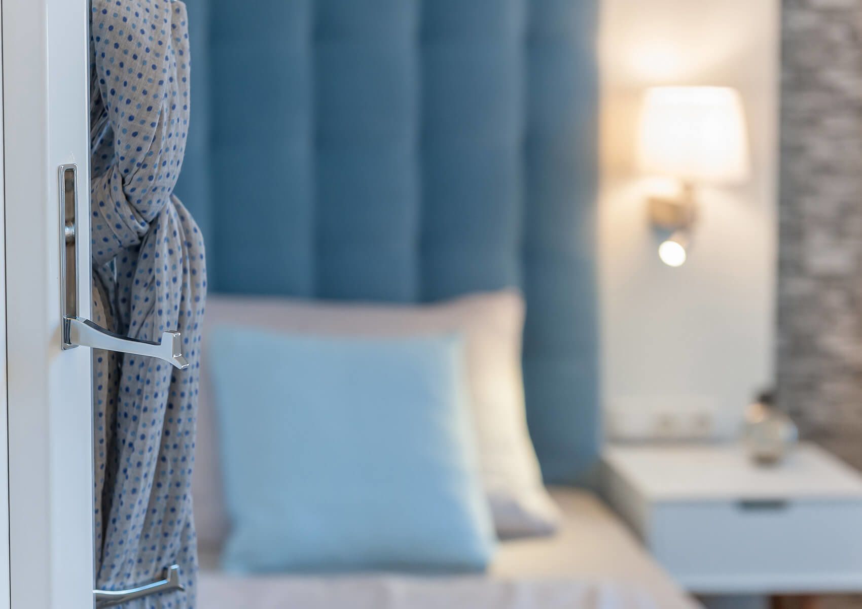 Camera d'albergo con un letto, un comodino, una lampada e un accappatoio appeso alla porta.