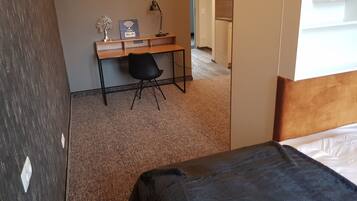 A hotel room with a bed, a desk with a chair, a lamp, and a sign indicating free Wi-Fi.