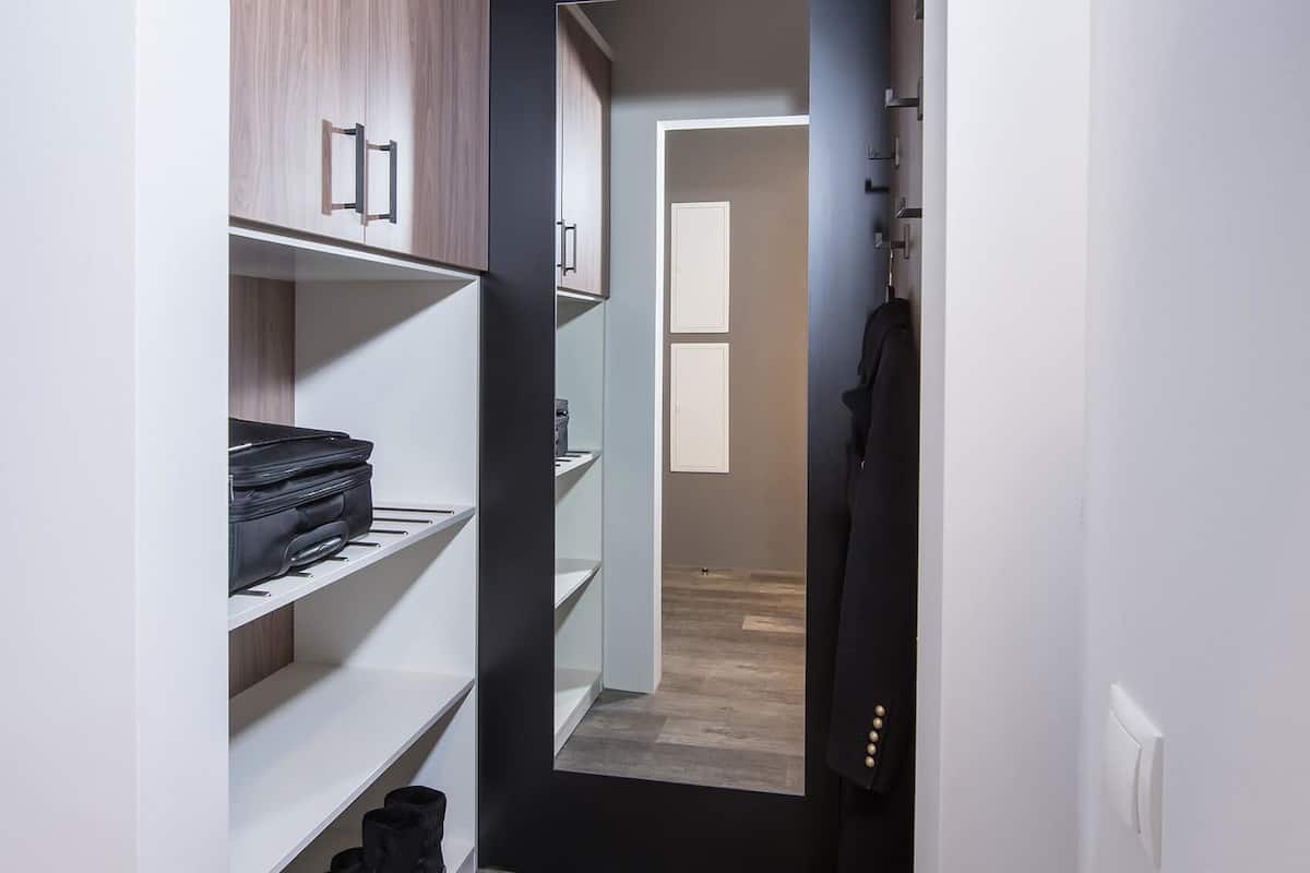 A narrow hallway with a wardrobe on the left, a coat rack on the right, and a door at the end leading to another room.