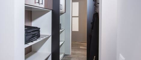 A narrow hallway with a wardrobe on the left, a coat rack on the right, and a door at the end leading to another room.
