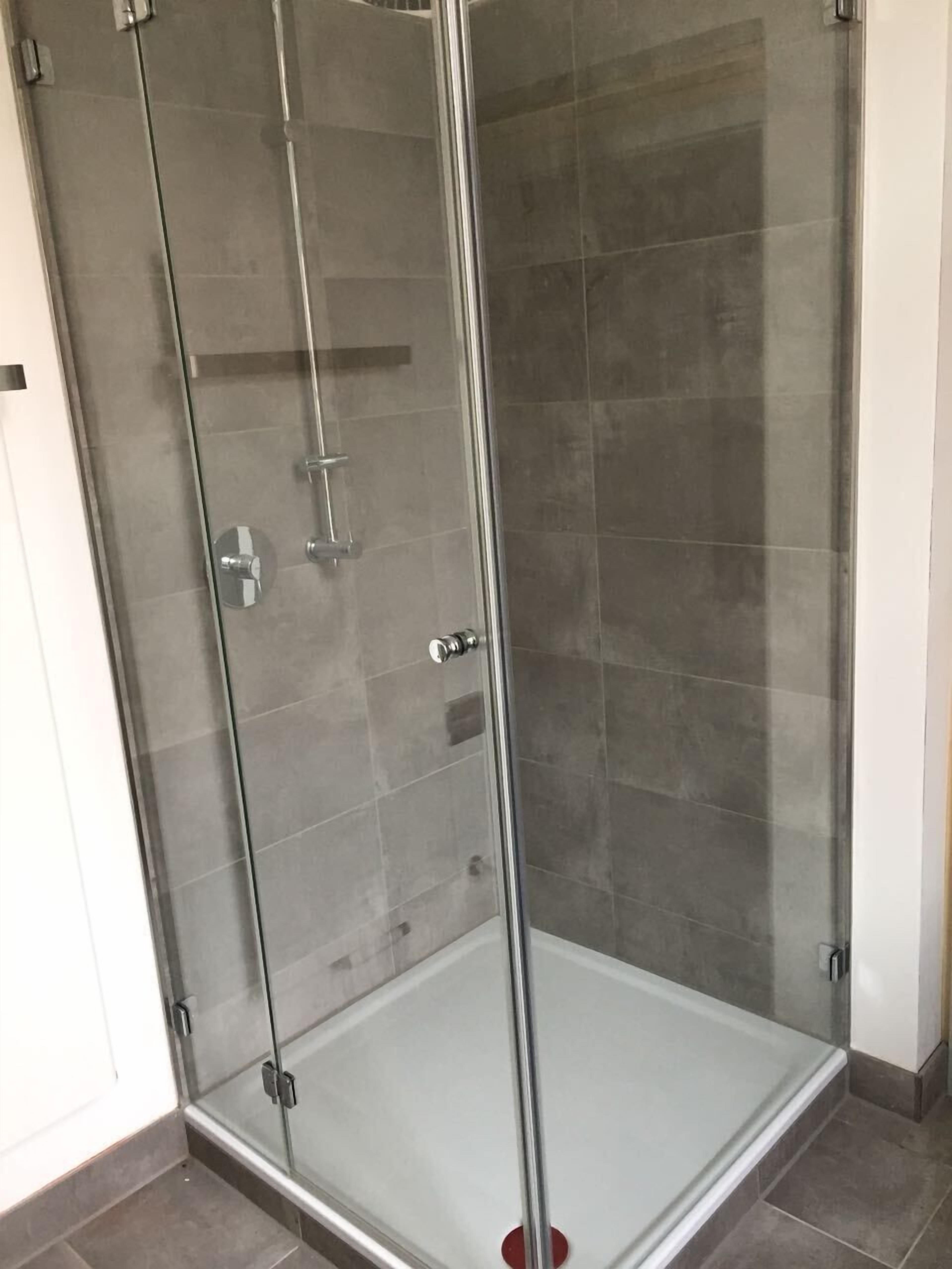 A glass-enclosed shower stall with a clear glass door, a showerhead, and a control panel.