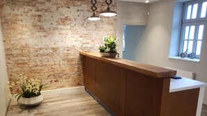A reception area with a brick wall, wooden reception desk, potted plants, and a window with a bicycle.