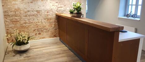 Un área de recepción con pared de ladrillo, mostrador de madera, plantas en macetas y un ventanal con una bicicleta.