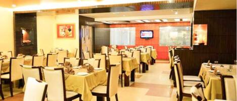 A restaurant with multiple tables and chairs, a television screen, and framed artwork on the walls.