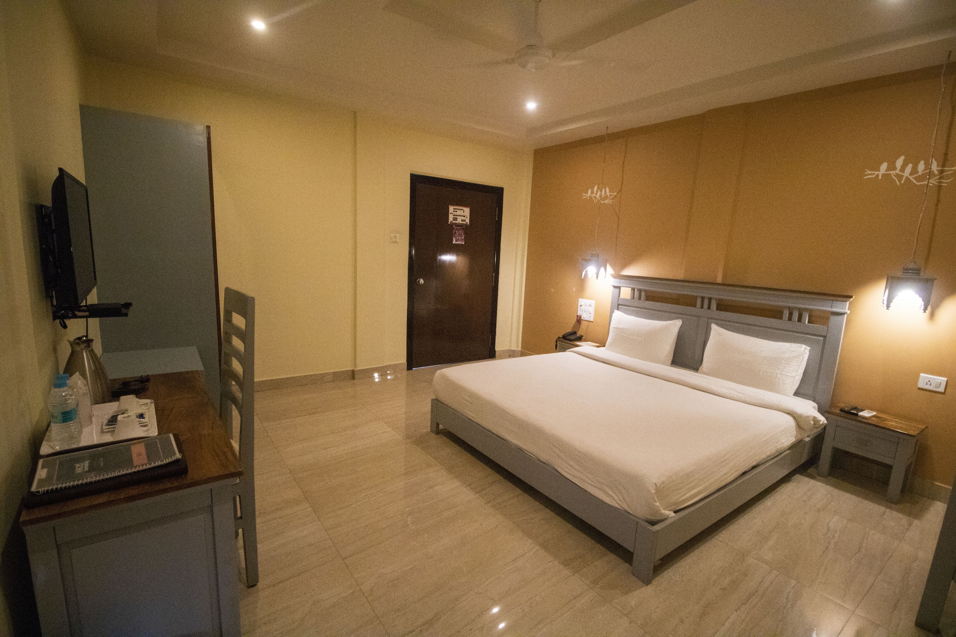Habitación de hotel con cama, mesitas de noche, escritorio con silla, televisor y puerta.