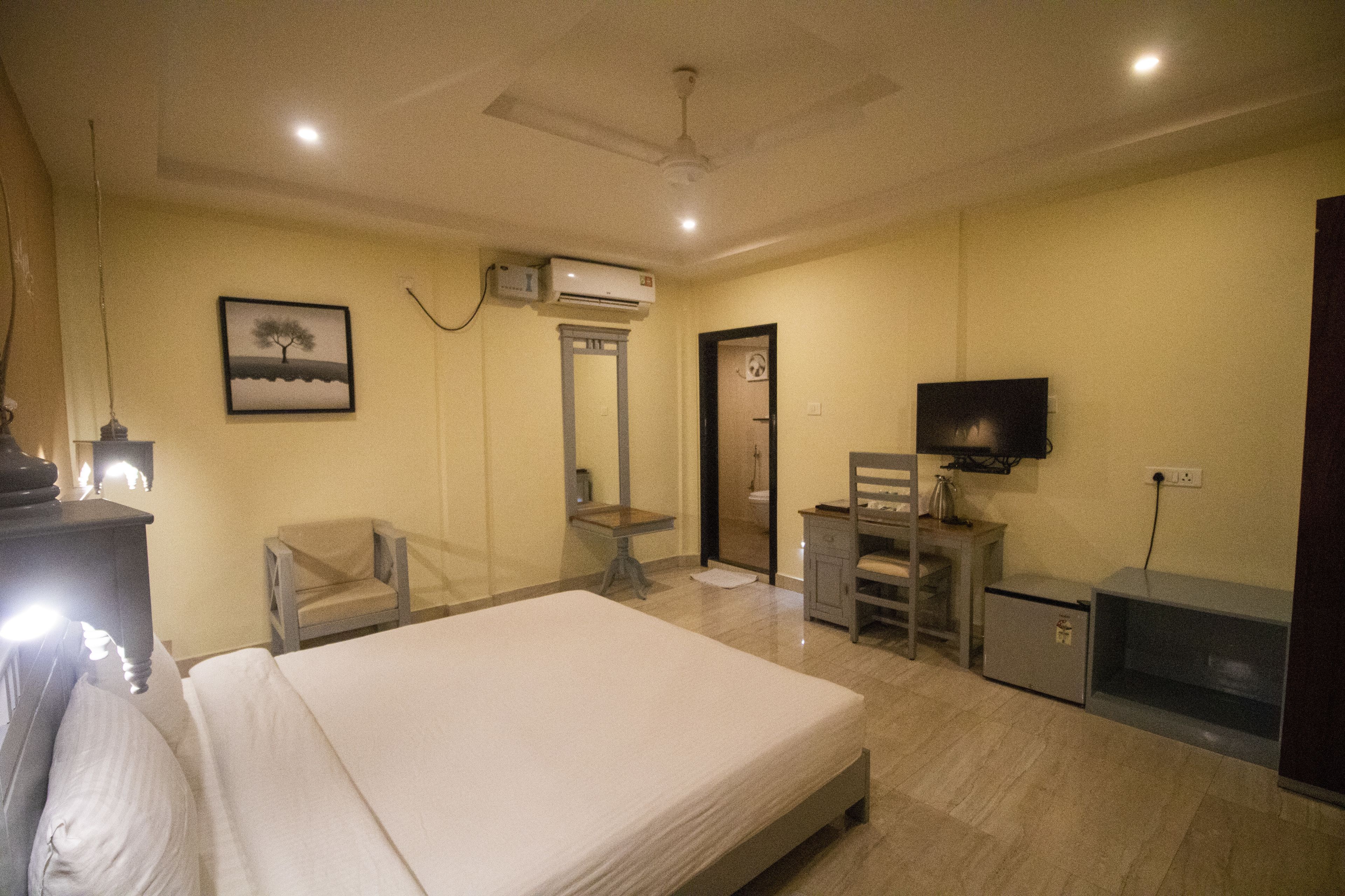 A hotel room with a bed, a desk, a chair, an air conditioner, a television, and a door.