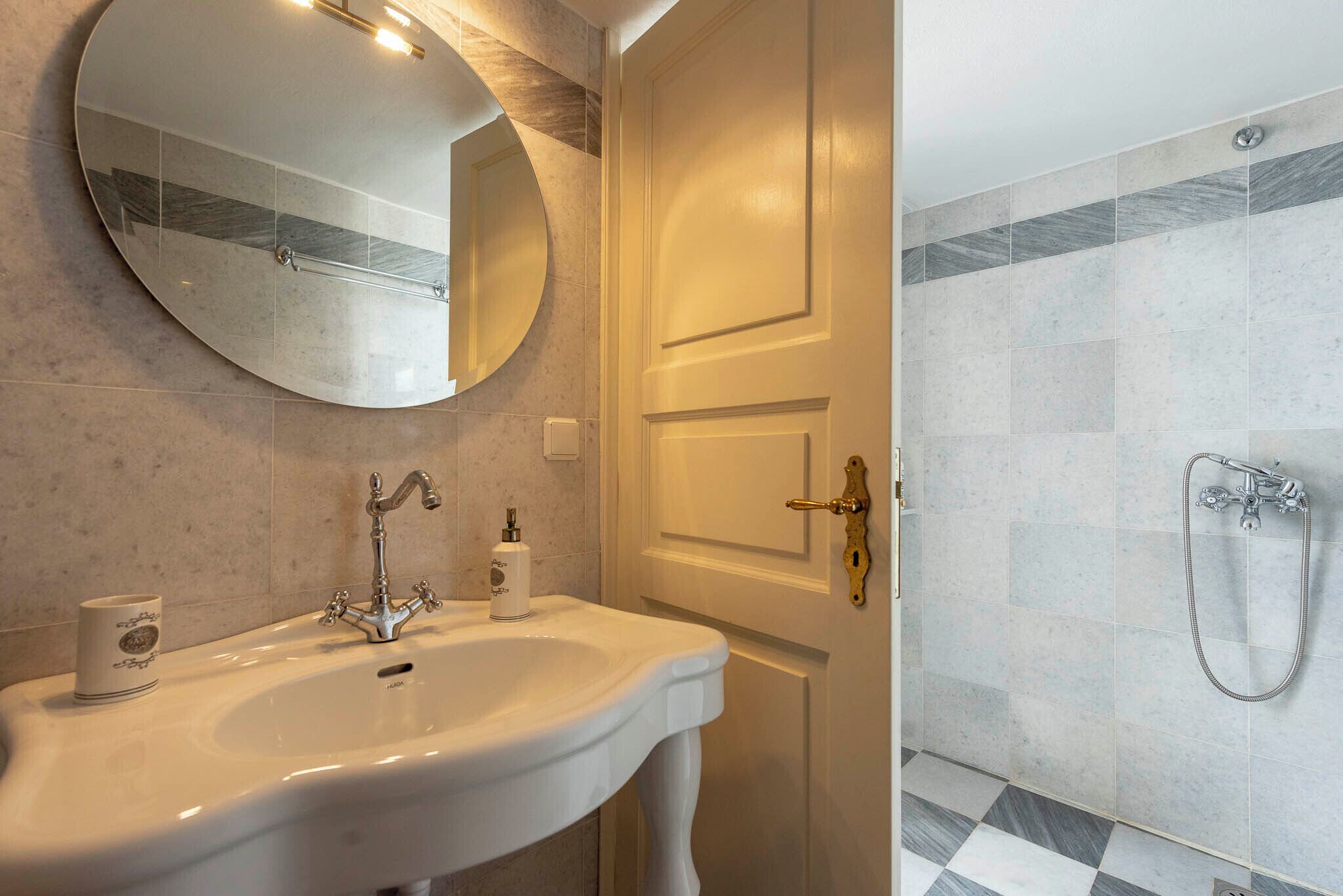 Un baño con lavamanos blanco, un espejo redondo y una zona de ducha con suelo de baldosas.