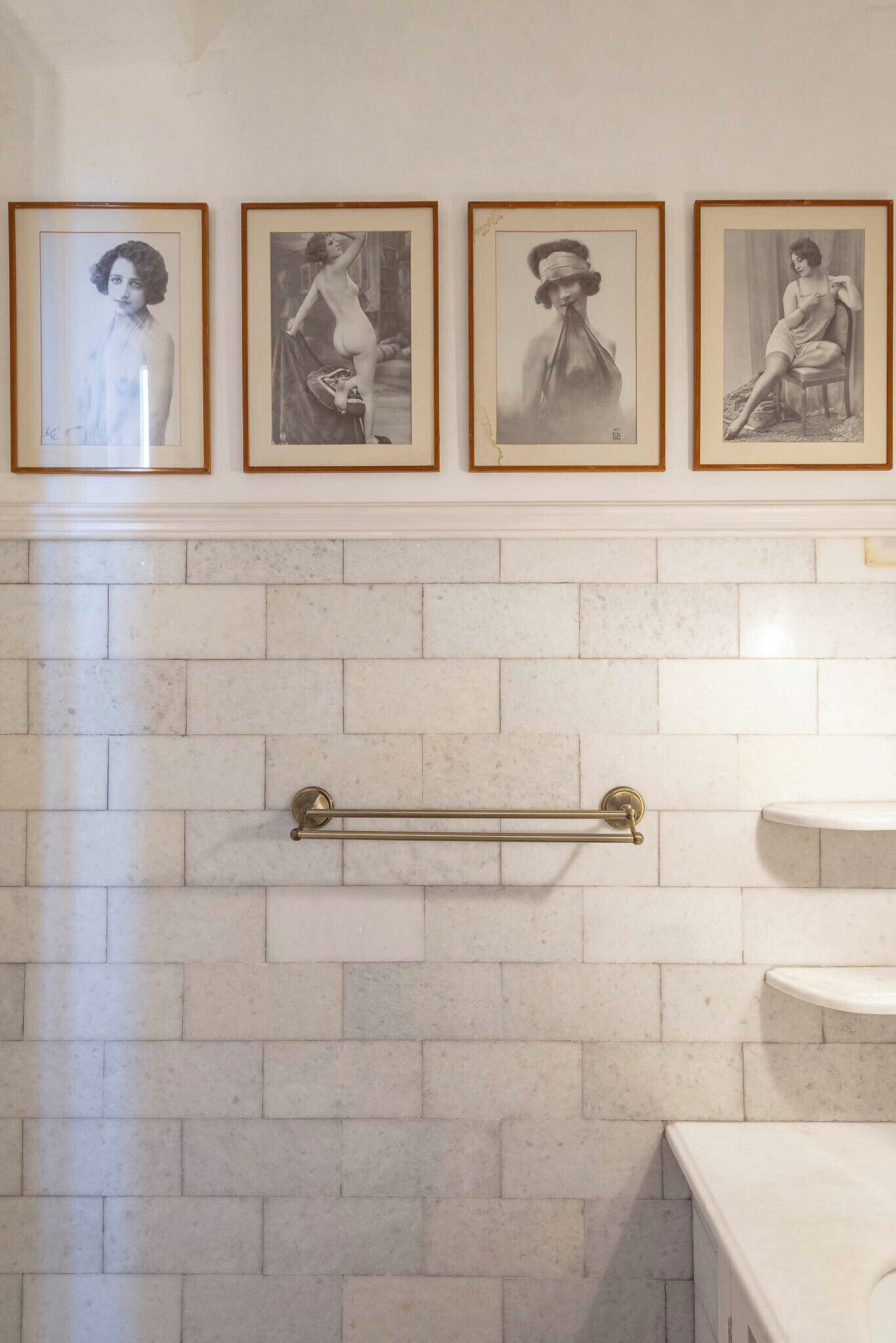 Un baño con paredes de azulejos blancos, un perchero y fotografías en blanco y negro enmarcadas.