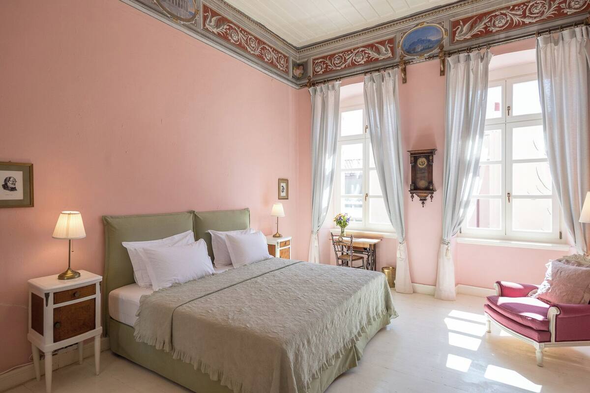 A bedroom with a bed, nightstands, a chair, a desk, and a window with curtains.