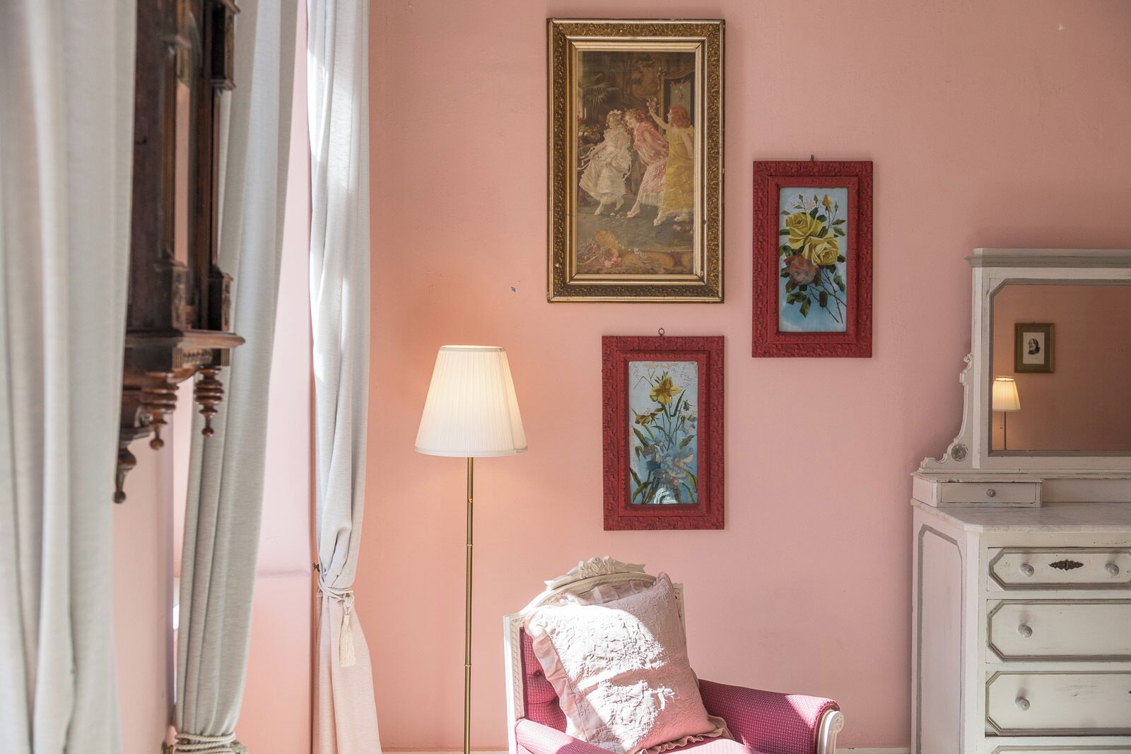 Una habitación con una pared rosa, un aparador blanco, una lámpara y tres obras de arte enmarcadas.