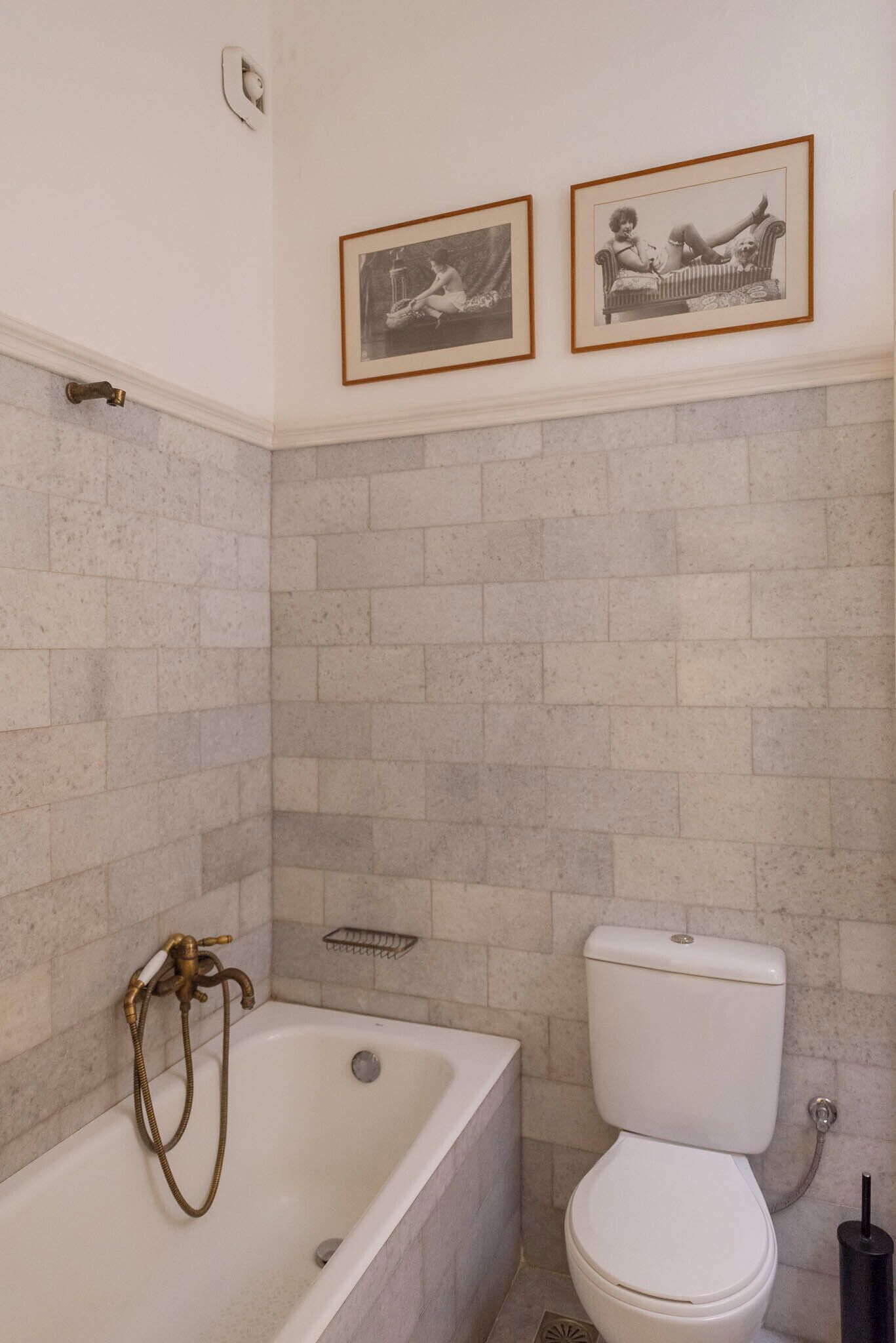 A bathroom with a bathtub, toilet, and two framed pictures on the wall.