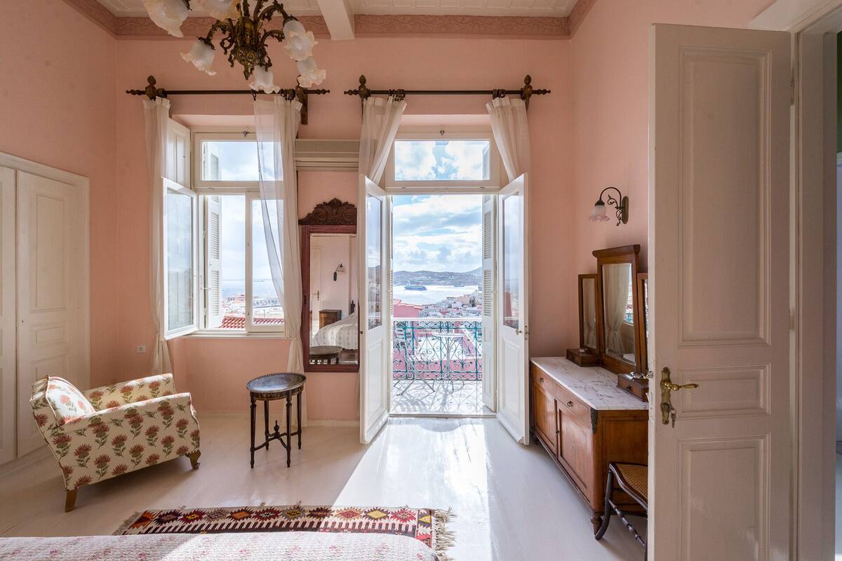 A bedroom with a large window, a bed, a dresser, and a chair.
