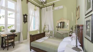 A room with a bed, a desk, and a chair. There is a window with curtains and a clock on the wall.