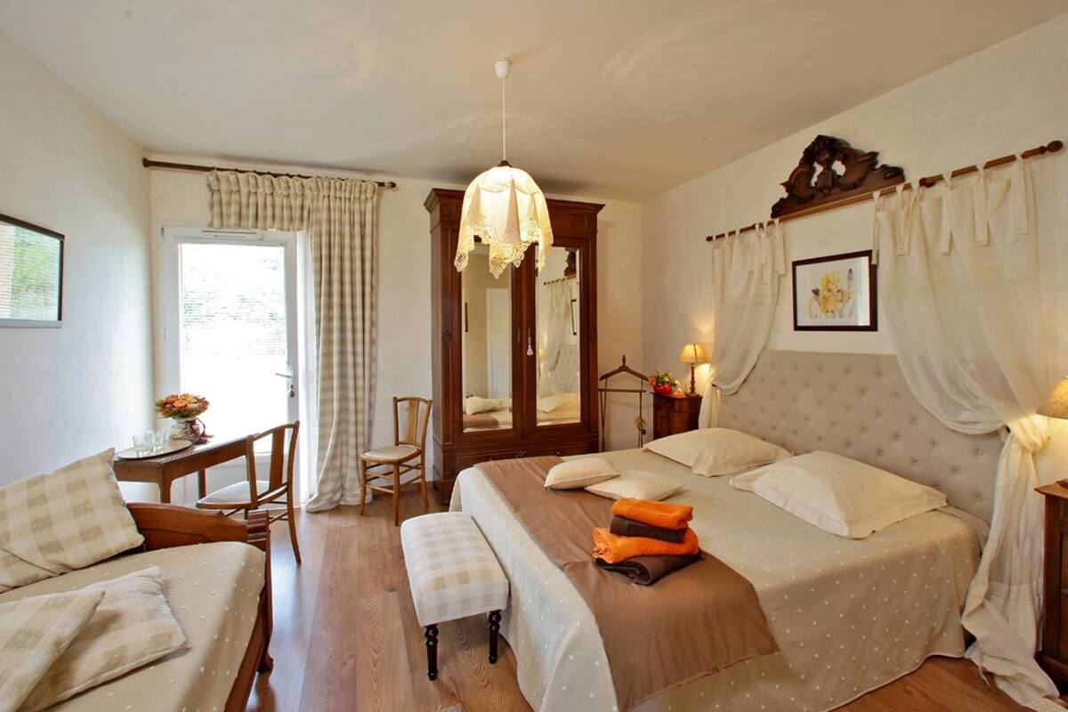 A bedroom with a large bed, a bedside table, a chair, and a window with curtains.