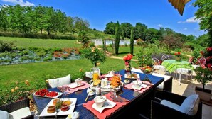 Un área de comedor al aire libre con una mesa preparada para el desayuno, rodeada de abundante vegetación y árboles.