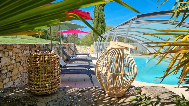 Zona de piscina con sillones de descanso, pared de piedra y lámpara de mimbre decorativa.