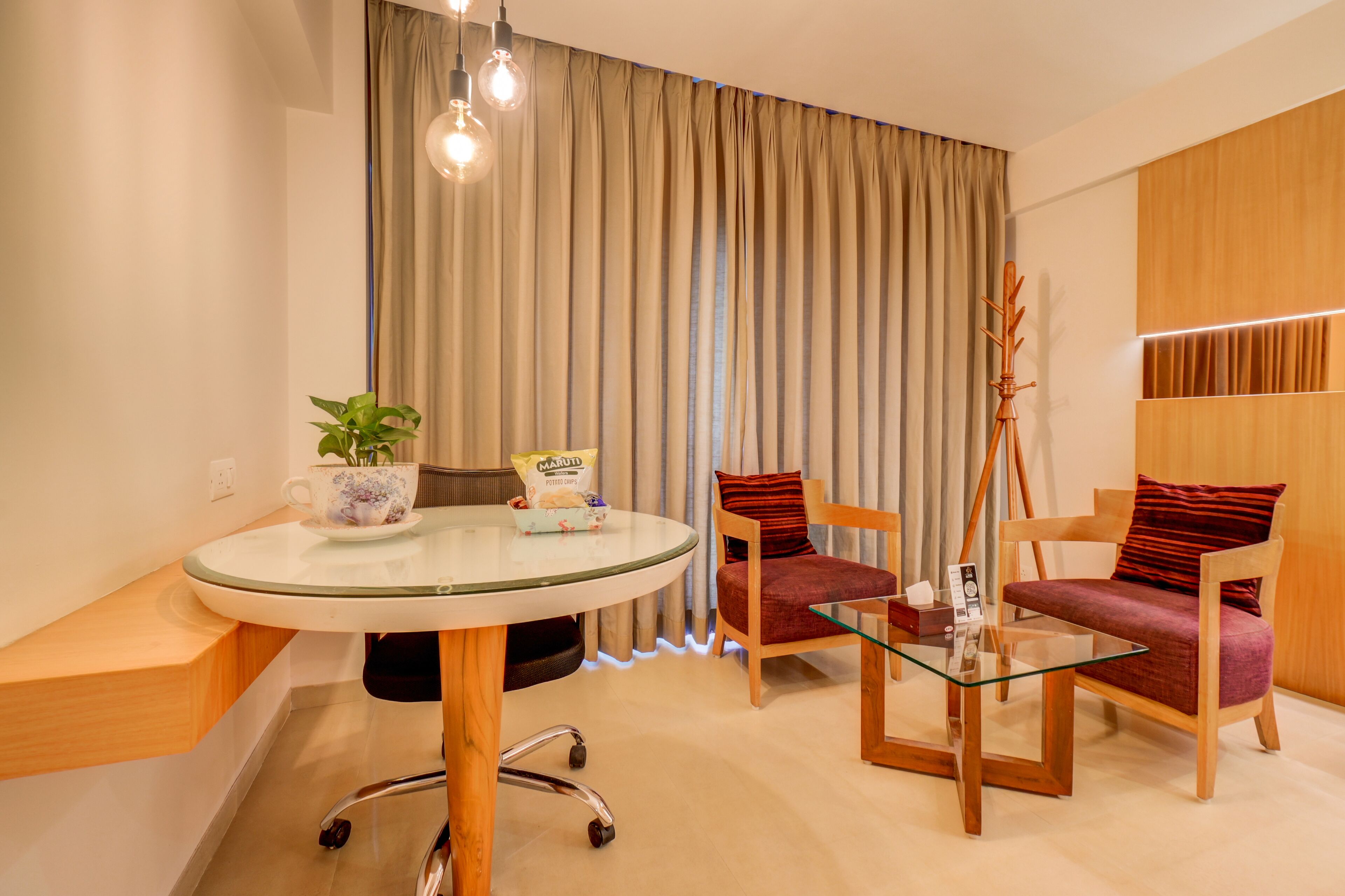 A modern living room with a glass table, two wooden chairs, a sofa, a potted plant, and a decorative item on the table.