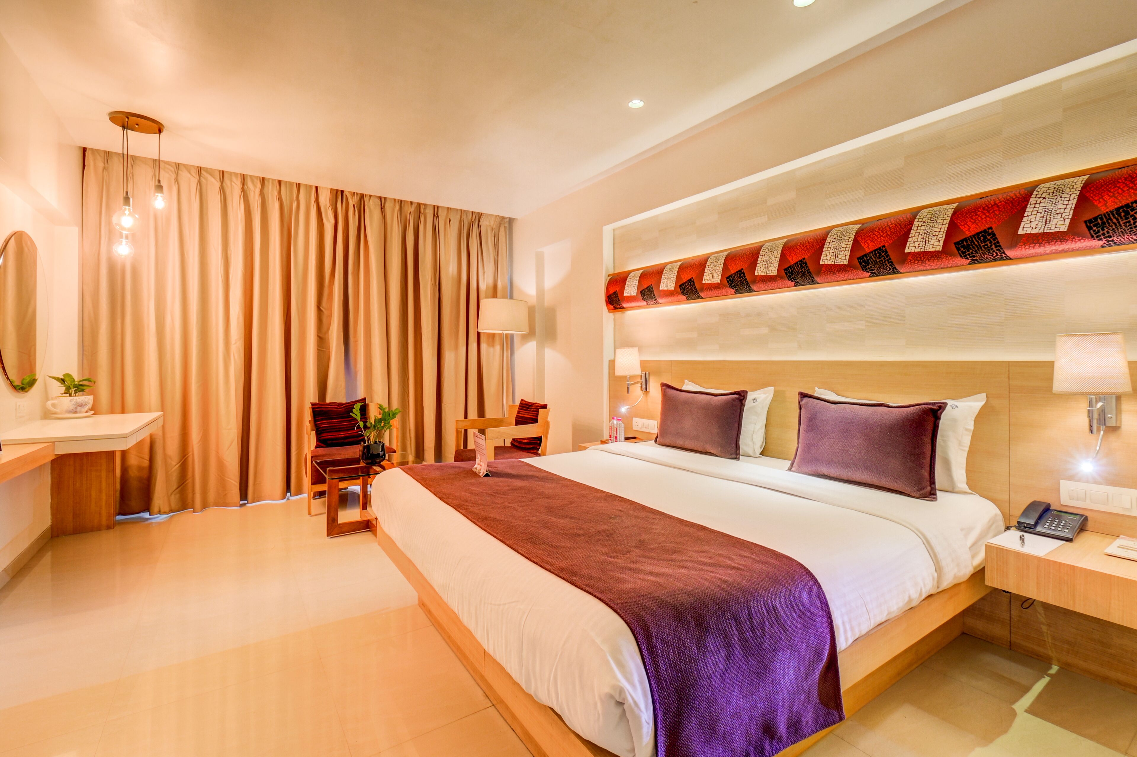 Una habitación de hotel moderna con una cama grande, una mesita de noche con lámpara, una silla y un escritorio con teléfono.