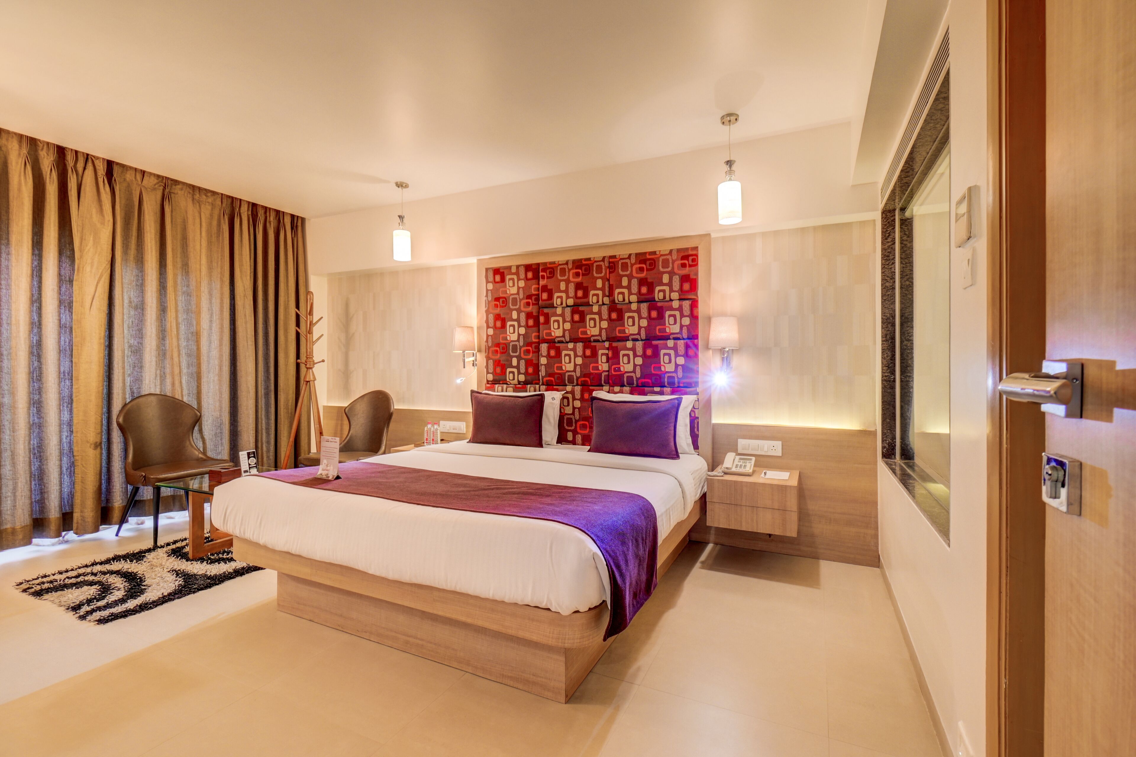 Une chambre d’hôtel moderne avec un grand lit, une table de chevet, une chaise, un miroir et un mur décoré d’un motif.
