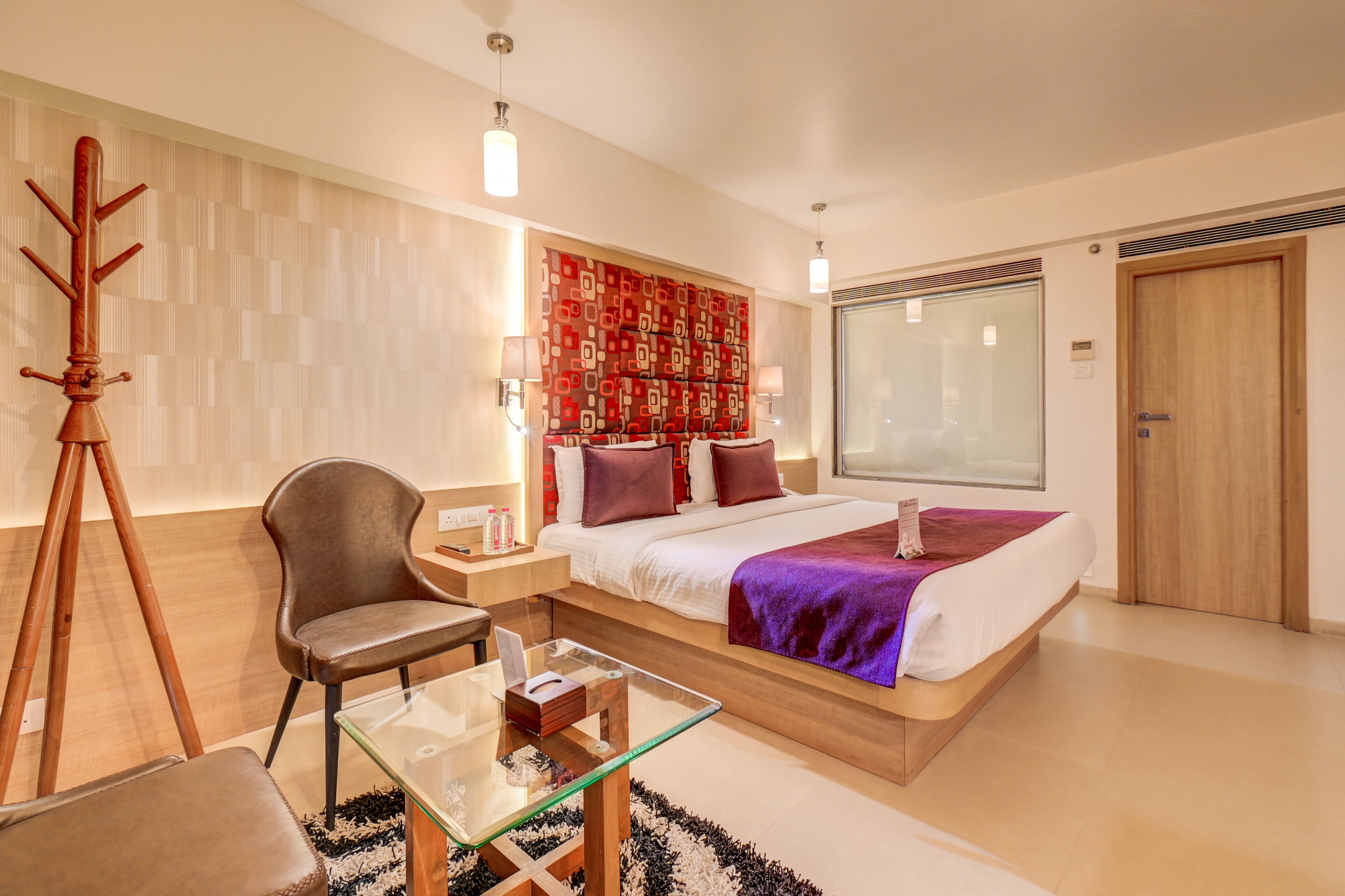 A modern hotel room with a large bed, a desk, a chair, and a tripod.