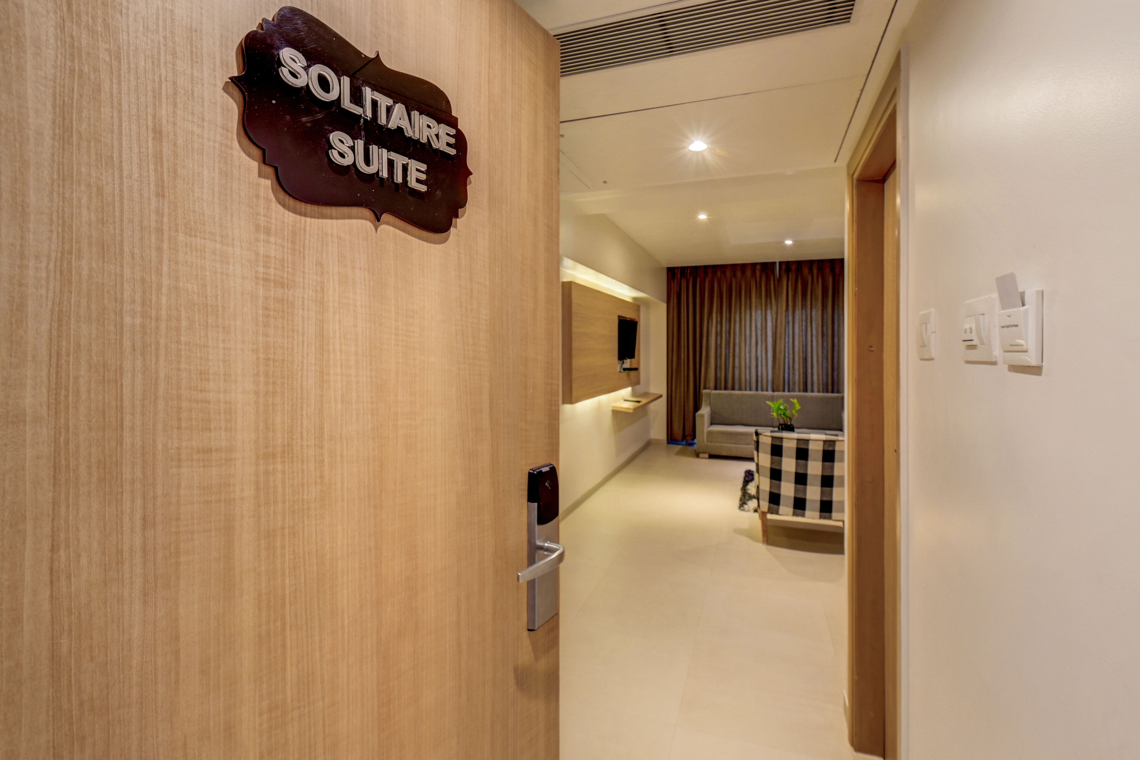 A hotel corridor with a sign for the Solitaire Suite, a reception area, a checkered table, and a sofa.