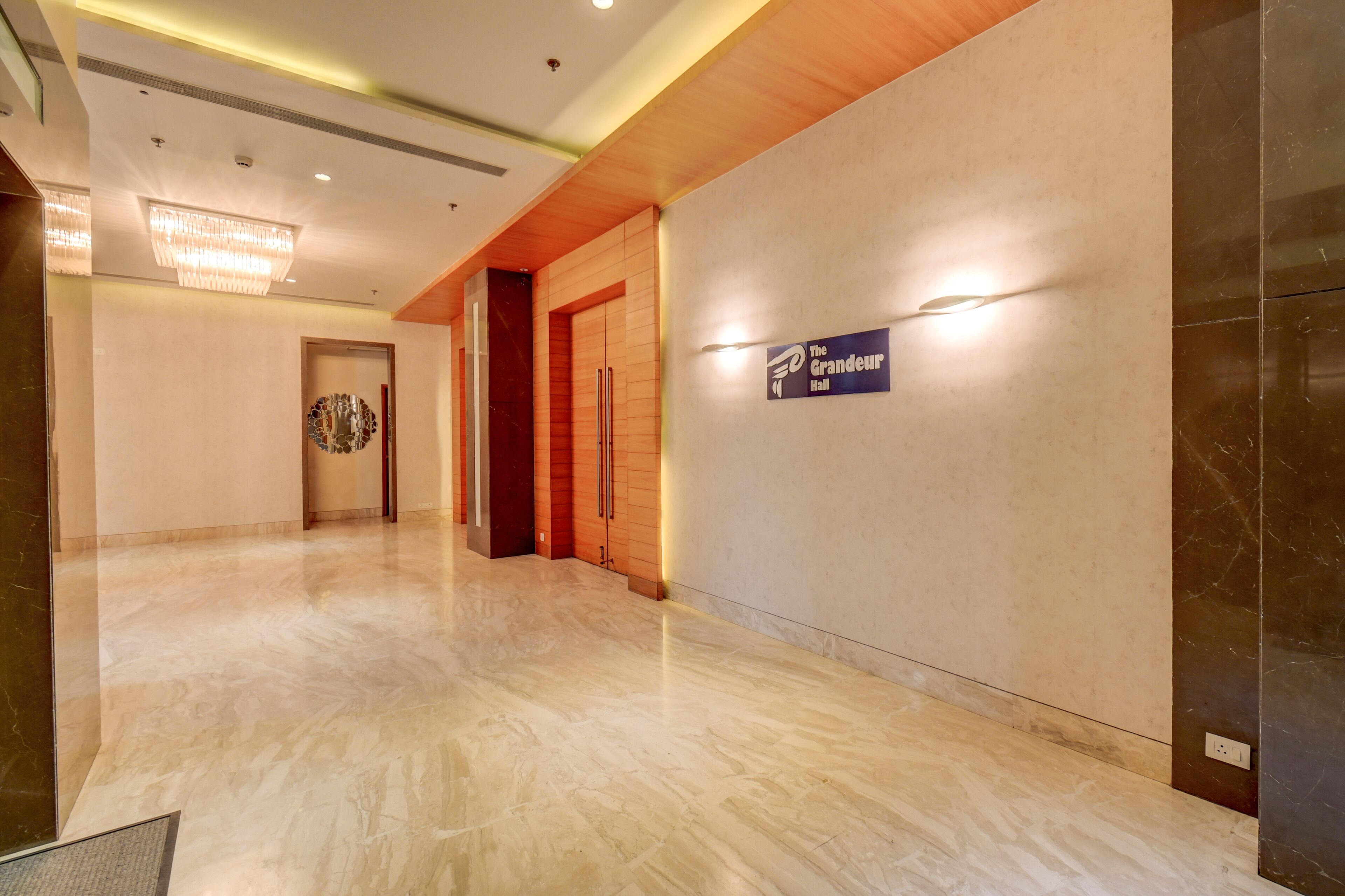 A hallway with a marble floor, wooden paneling, a chandelier, and a sign for "The Grandeur Hall".