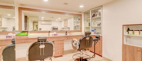 A modern bathroom with two barber chairs, a large mirror, and a shelf with toiletries.