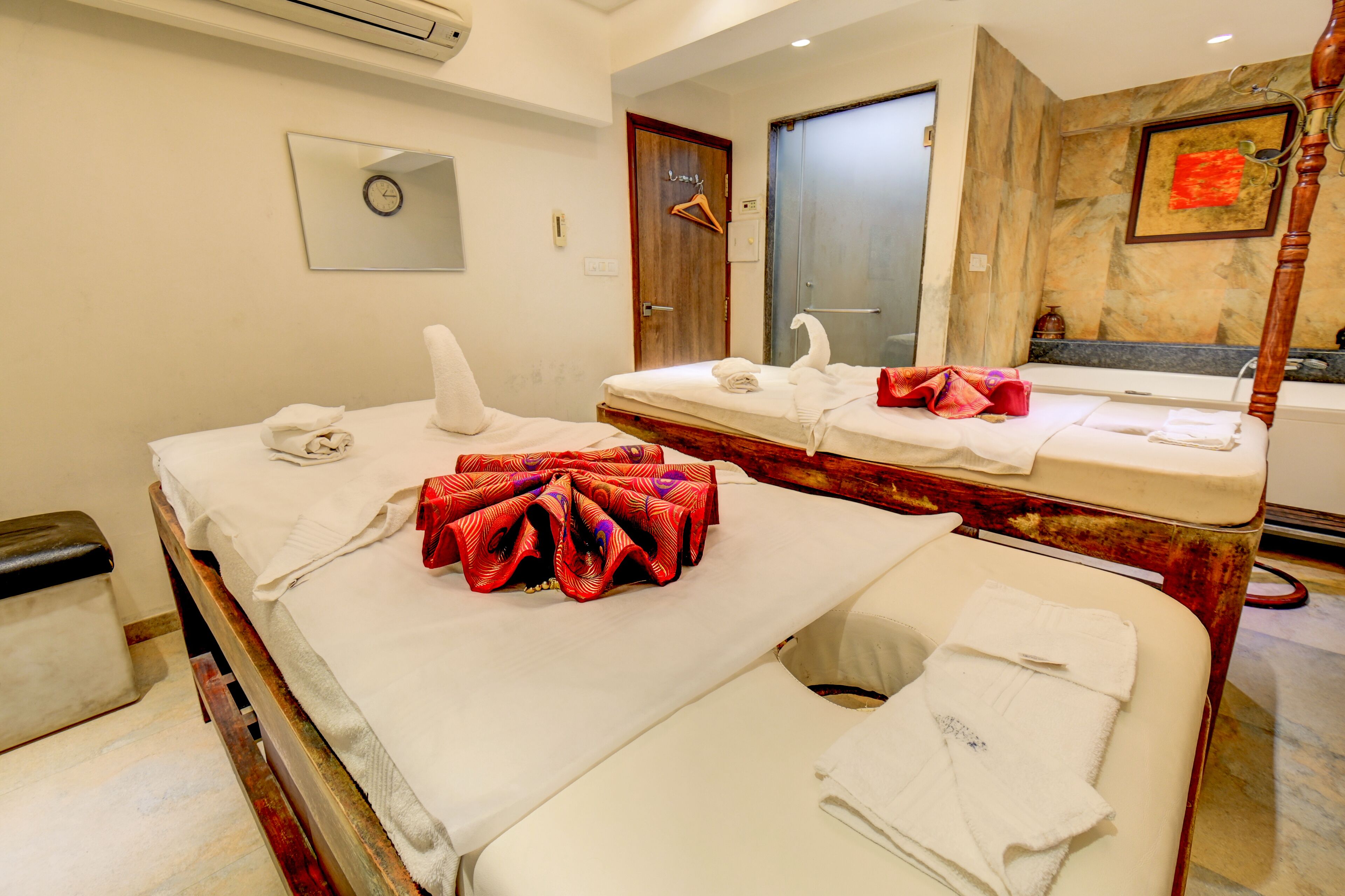 Habitación de hotel con una mesa de masaje, una bañera, un espejo y un reloj en la pared.