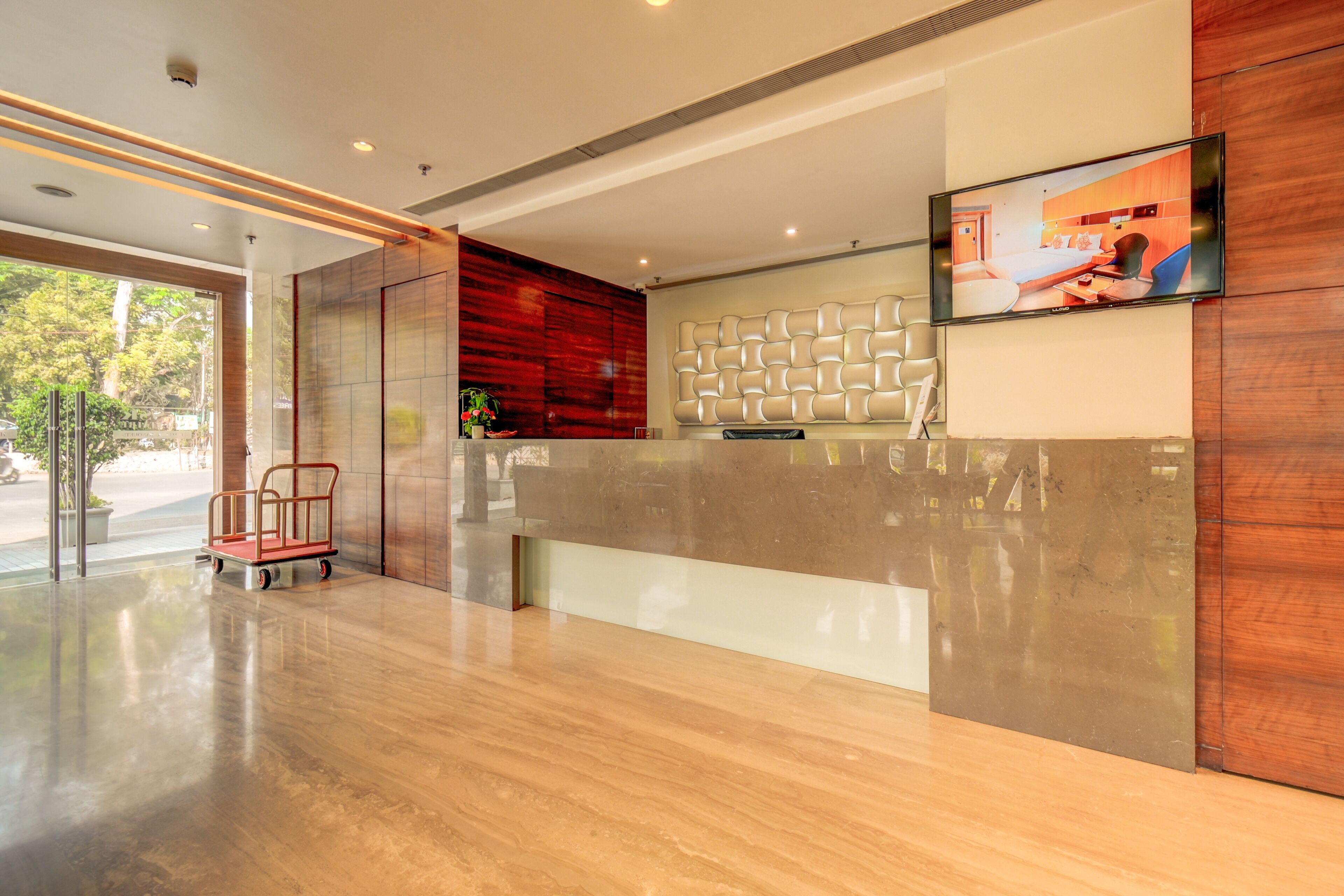 A modern reception area with a polished wooden floor, a reception desk, a mounted television, and a cart.