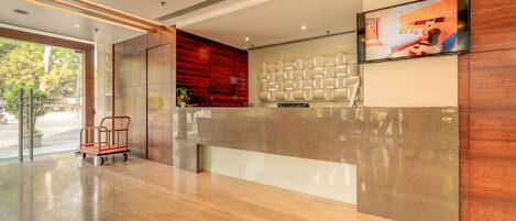 A modern reception area with a polished wooden floor, a reception desk, a mounted television, and a cart.