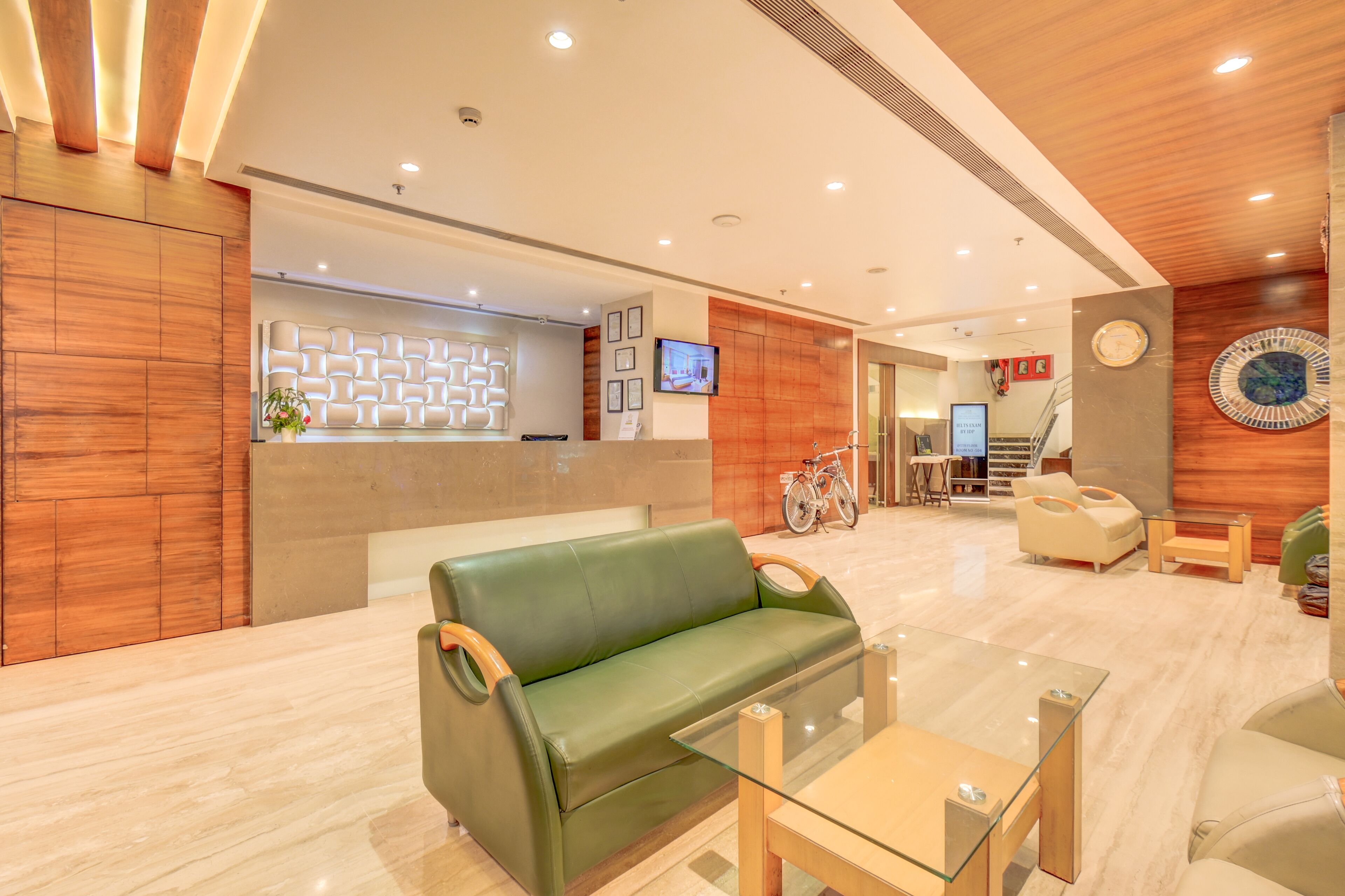 A modern hotel lobby with a reception desk, green leather sofa, and a glass coffee table.