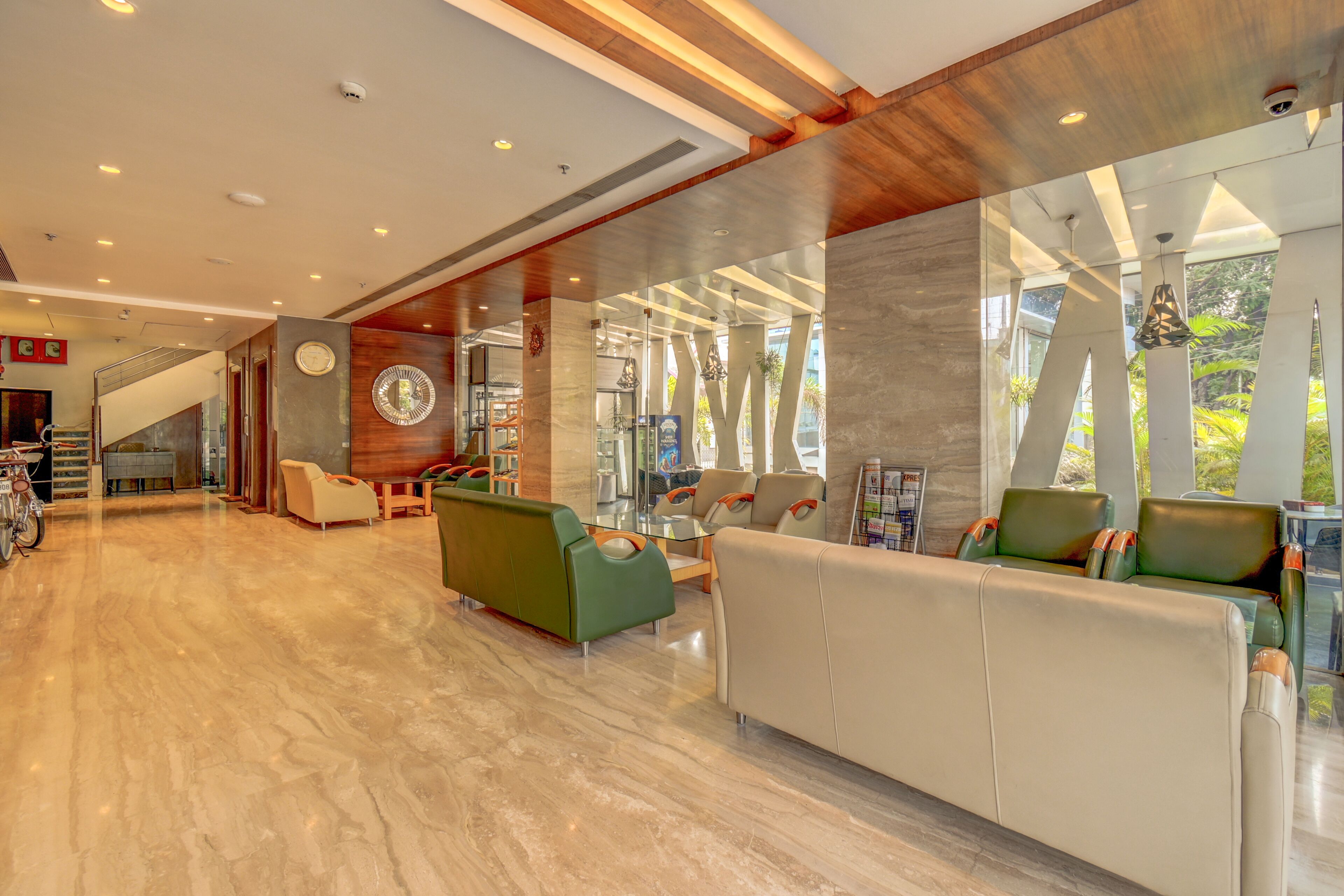 A modern lobby with a marble floor, green and beige seating, a staircase, and large windows.