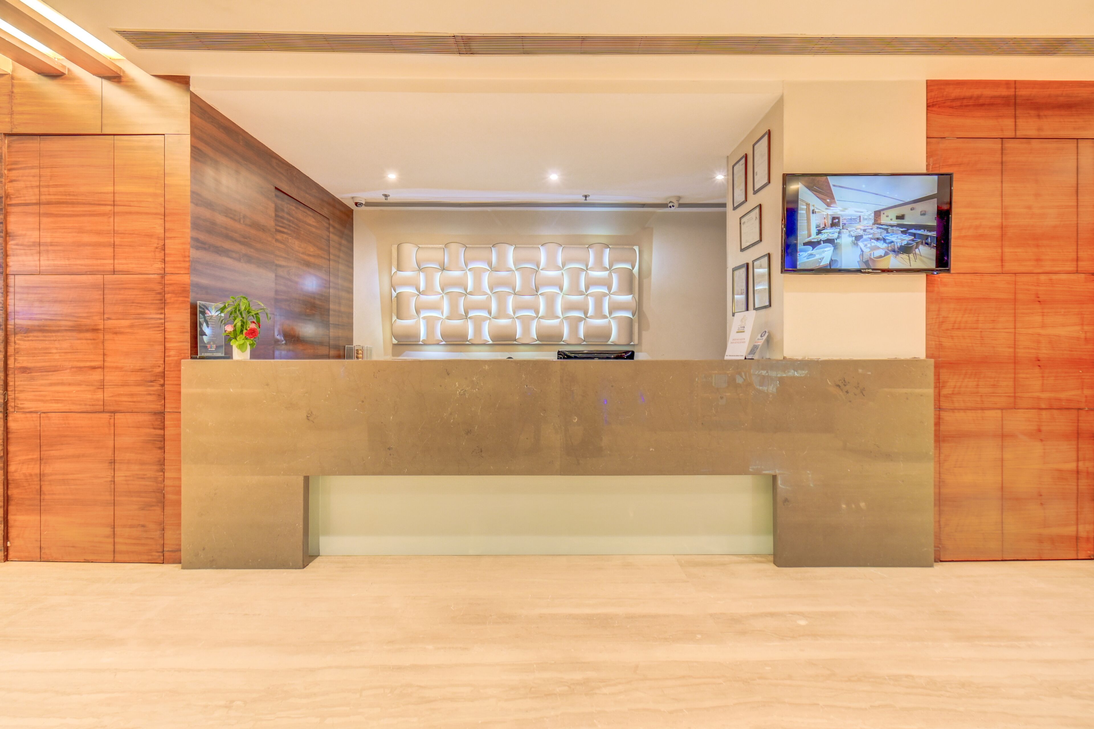 A reception area with a modern design, featuring a wooden reception desk, a decorative wall panel, and a mounted television.