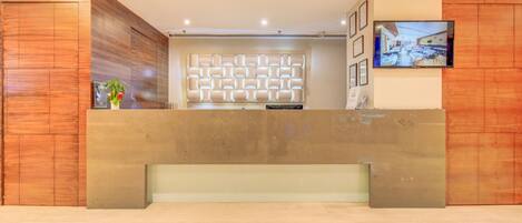 A reception area with a modern design, featuring a wooden reception desk, a decorative wall panel, and a mounted television.