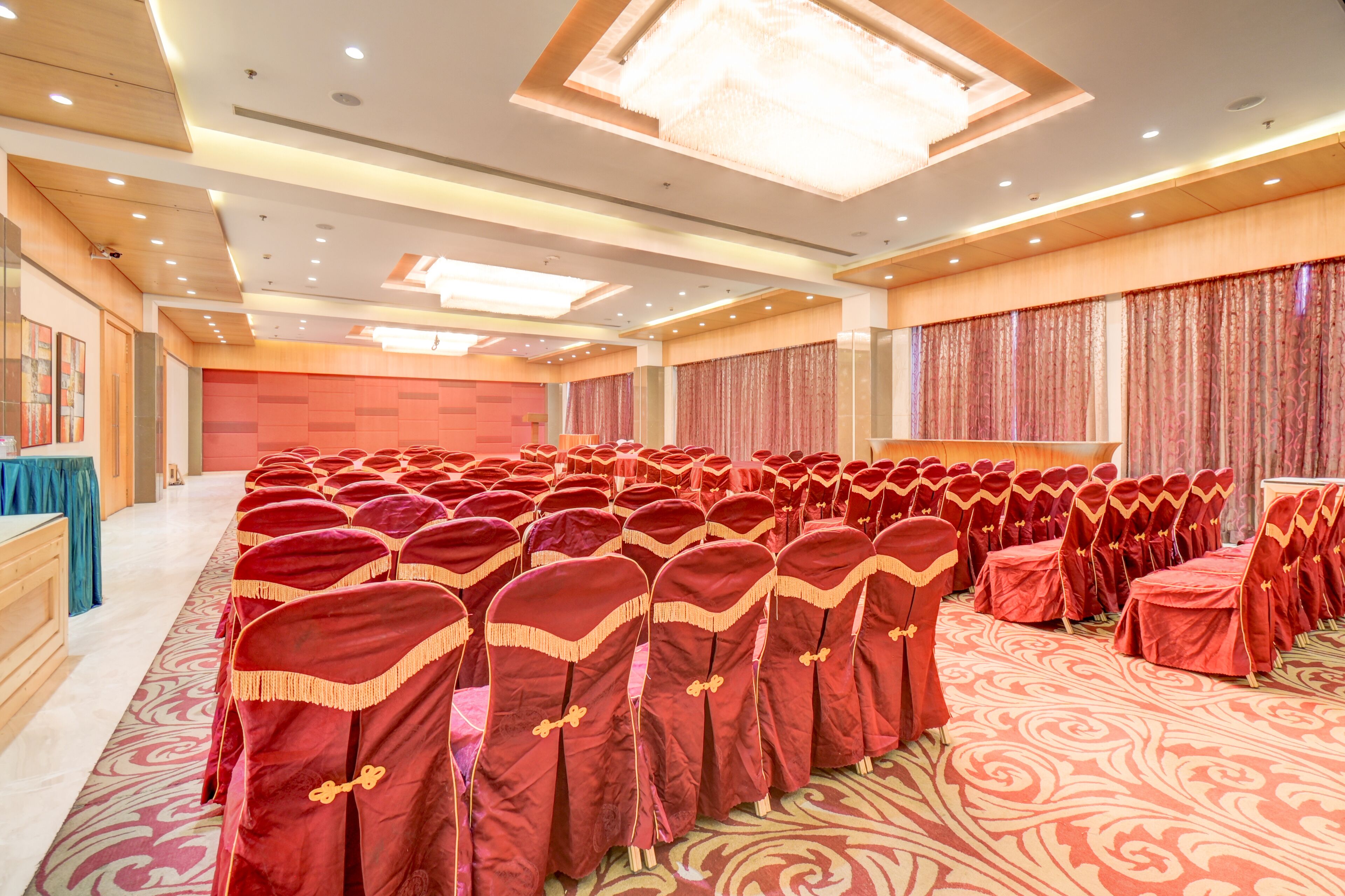 A large conference room with rows of red-covered chairs and a stage.