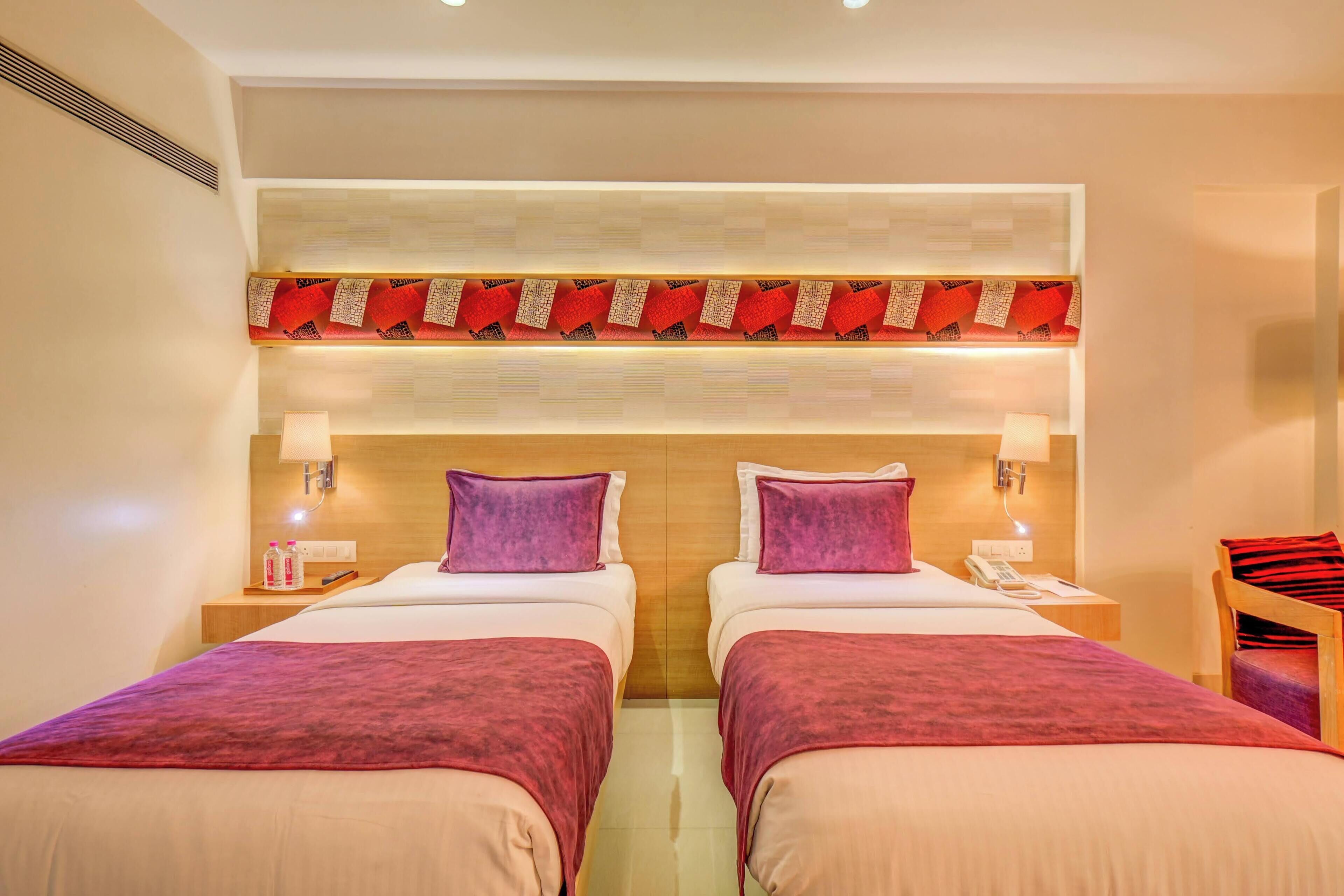 A hotel room with two beds, a wooden headboard, and a red decorative panel above the beds.