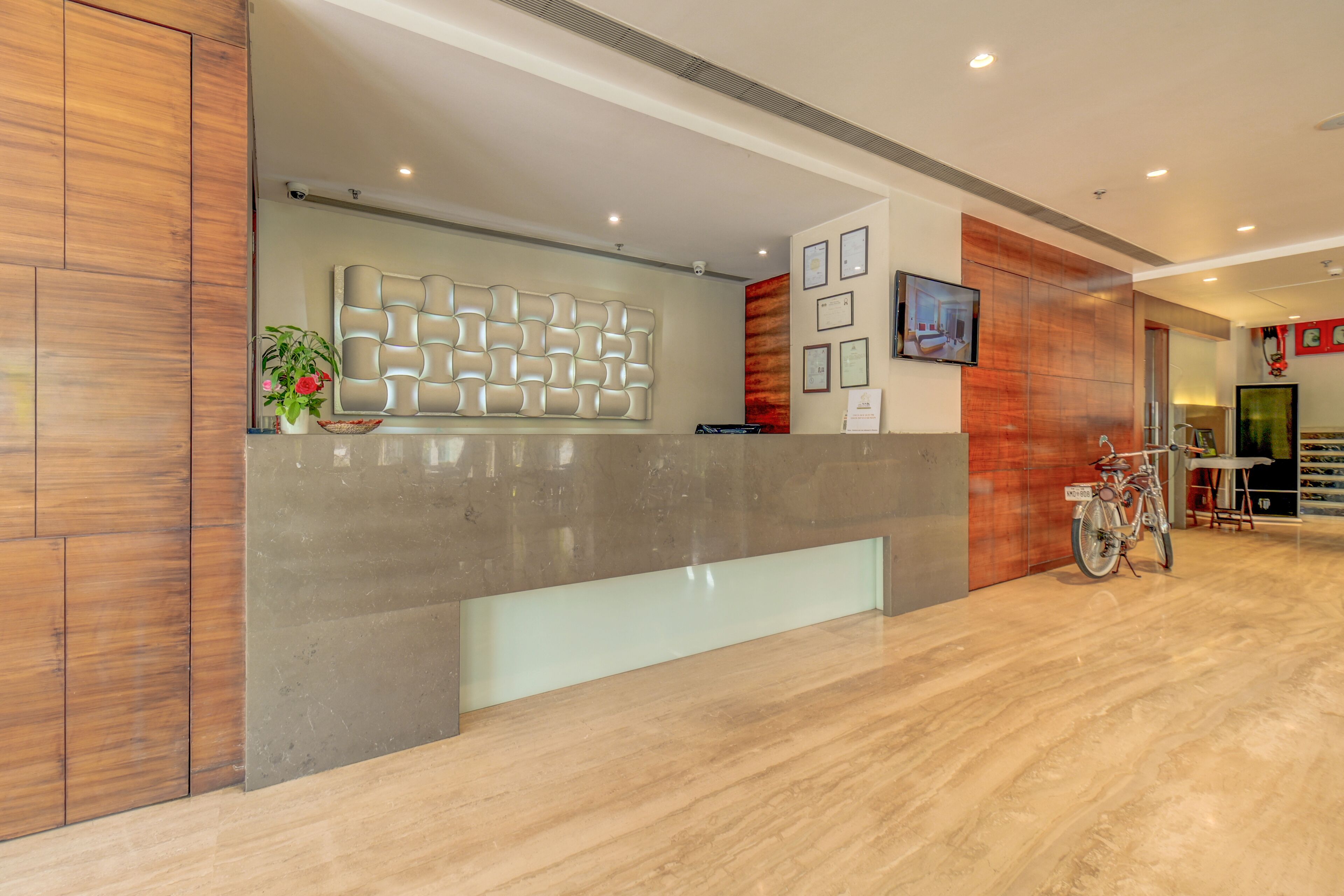 A reception area with a modern design, featuring a marble reception desk, a wall-mounted decorative panel, and a mounted television.