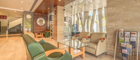 A lobby with a glass coffee table, green and beige seating, a reception desk, and a magazine rack.