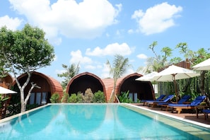 A pool area with lounge chairs and umbrellas, surrounded by trees and a clear sky. - AloraVilla (Senggigi)