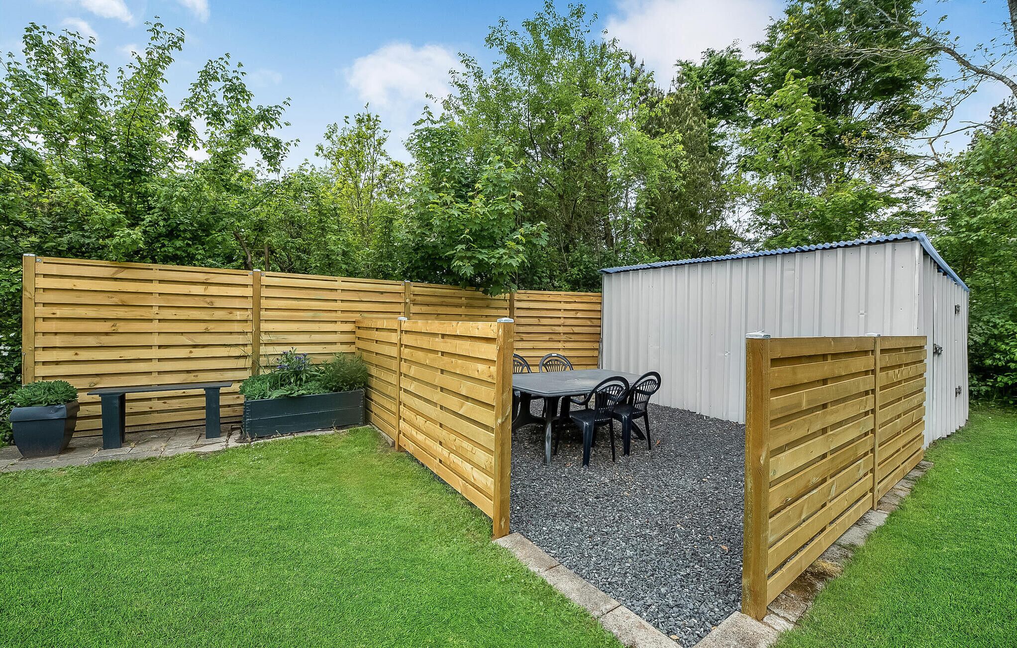 A fenced backyard with a wooden bench, a table with chairs, and a shed.