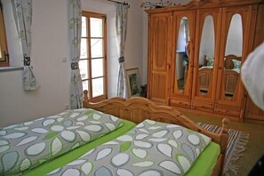 Een slaapkamer met twee bedden, een houten garderobe en een raam met gordijnen.