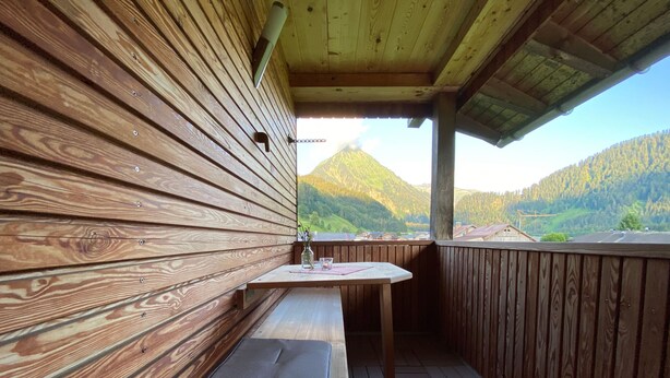 Una terraza de madera con una mesa y banco, con vistas a un paisaje montañoso.