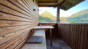 Een houten terras met een tafel en bank, met uitzicht op een bergachtig landschap.
