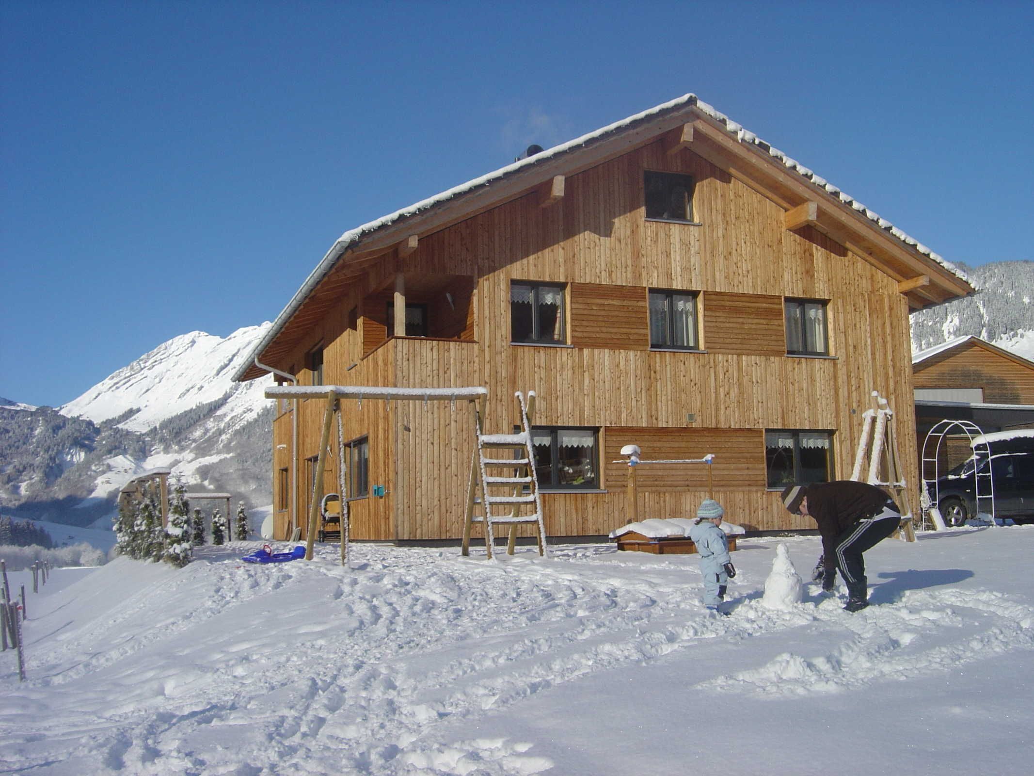 Een houten chalet met veel ramen, een schuin dak en een met sneeuw bedekte grond.