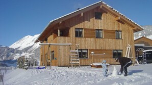 Una cabaña de madera con múltiples ventanas, techo inclinado y suelo cubierto de nieve.