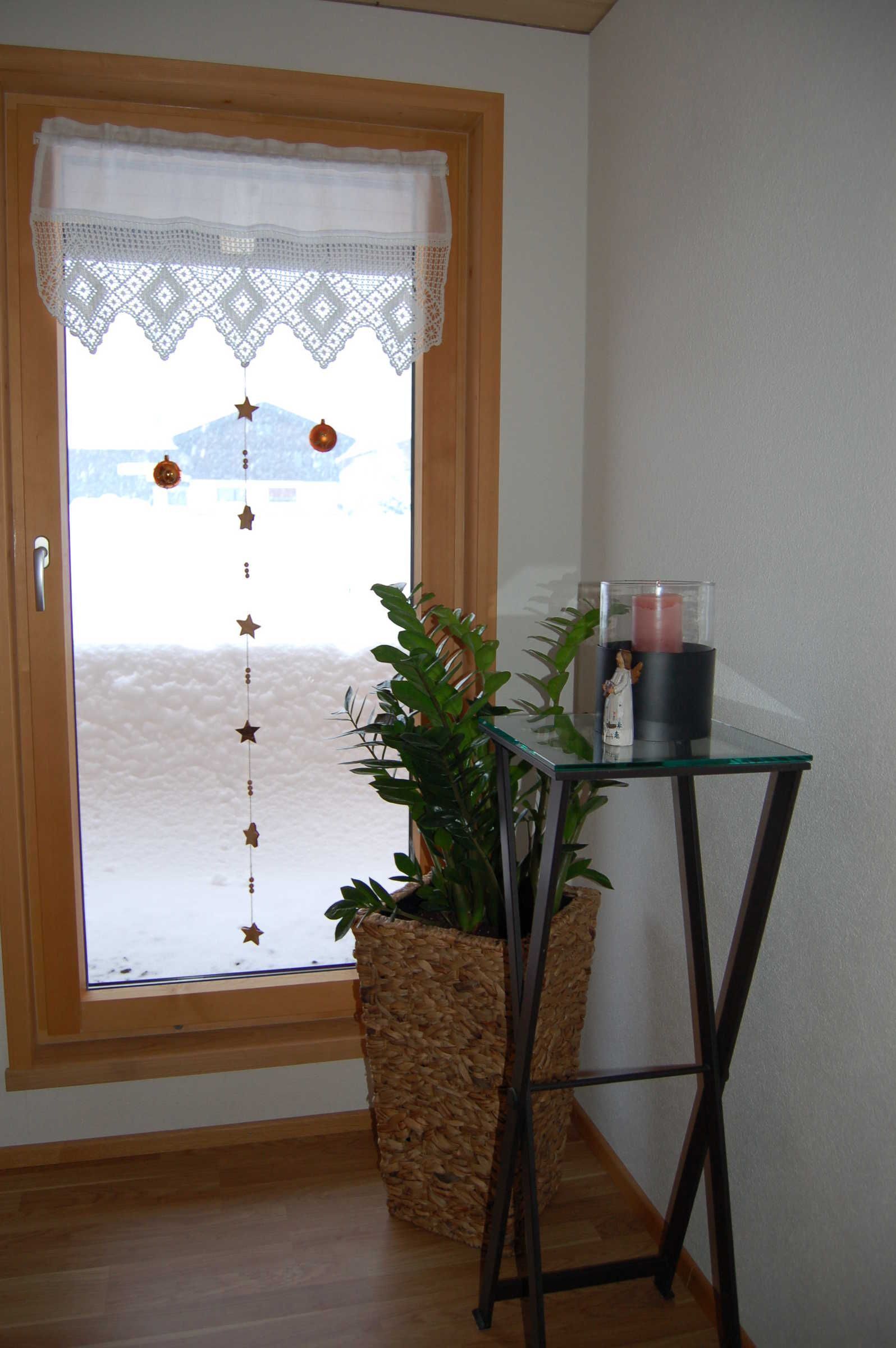 Een kamer met een raam met houten kader, een glazen tafel met een kaars en een potplant.