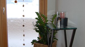 Una habitación con ventana de madera, una mesa de vidrio con una vela y una planta en maceta.