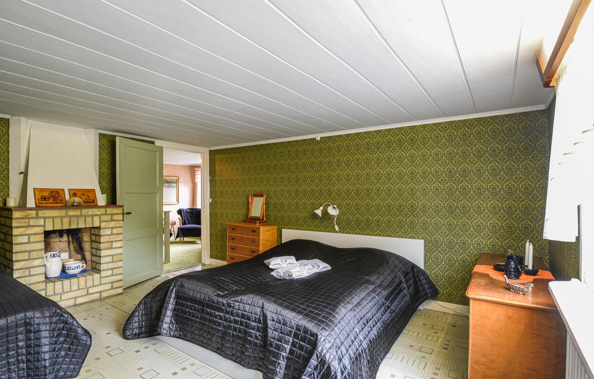 Een slaapkamer met twee bedden, een bakstenen open haard, een dressoir en een groene, patroonbehangde muur.